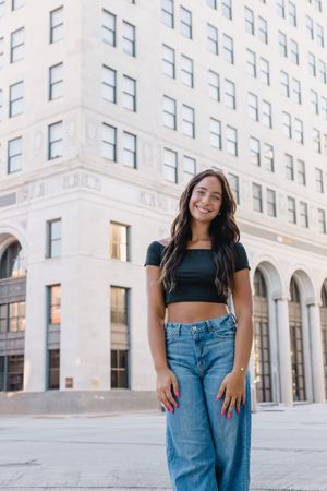 Stylish outfit with black crop top and wide-leg jeans photographed against modern urban architecture in natural light.