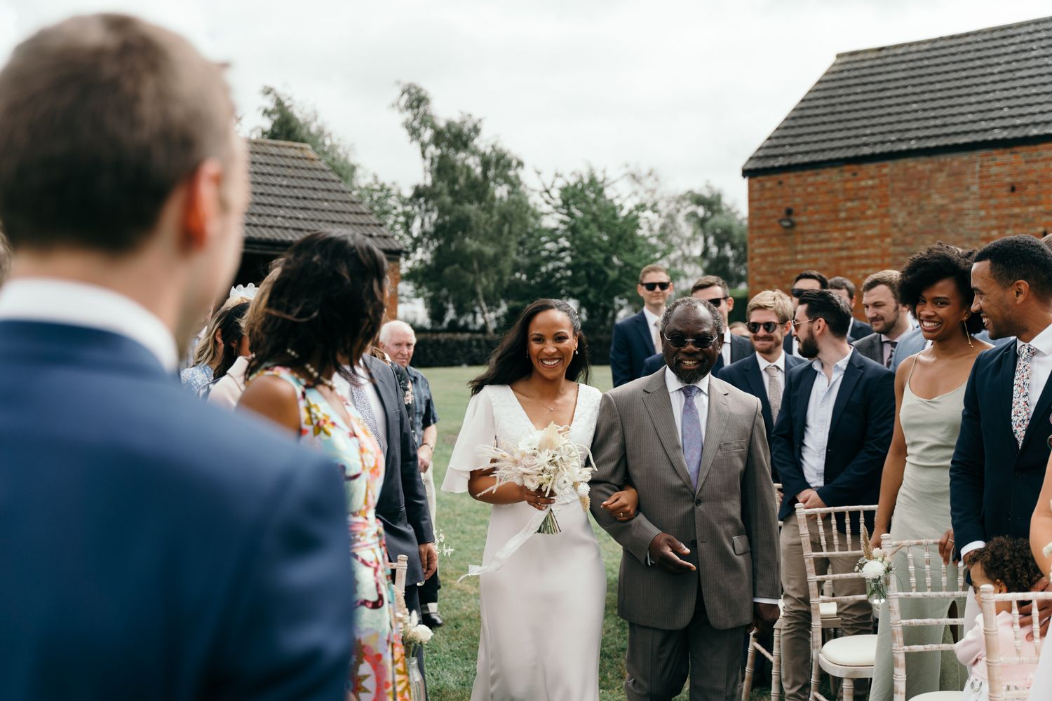A group of wedding guests gathered outdoors at a rustic venue during a daytime celebration.