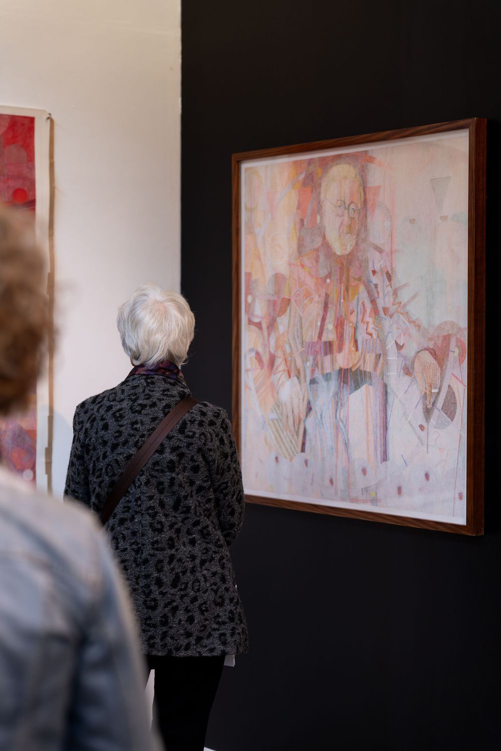 Elderly woman with white hair viewing abstract portrait painting in a gallery exhibition.