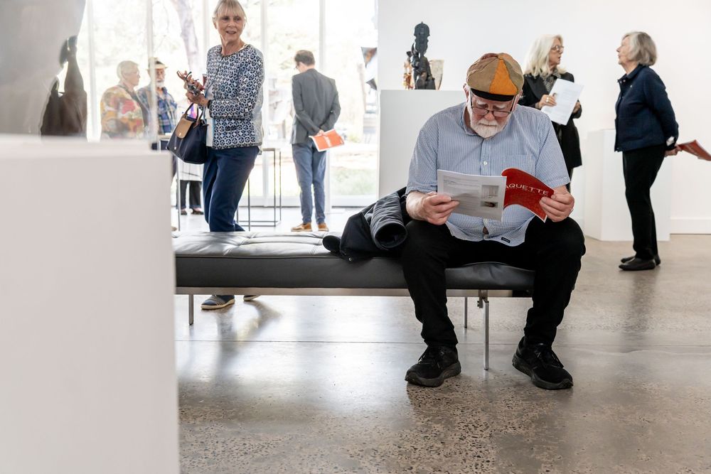 People sitting and standing in a minimalist white gallery or museum space.