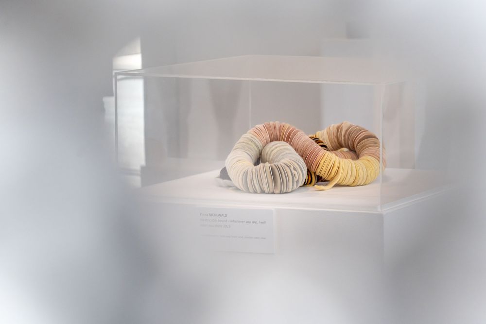 Three knitted yarn balls in beige and cream colors displayed in a minimalist white cube shelf.