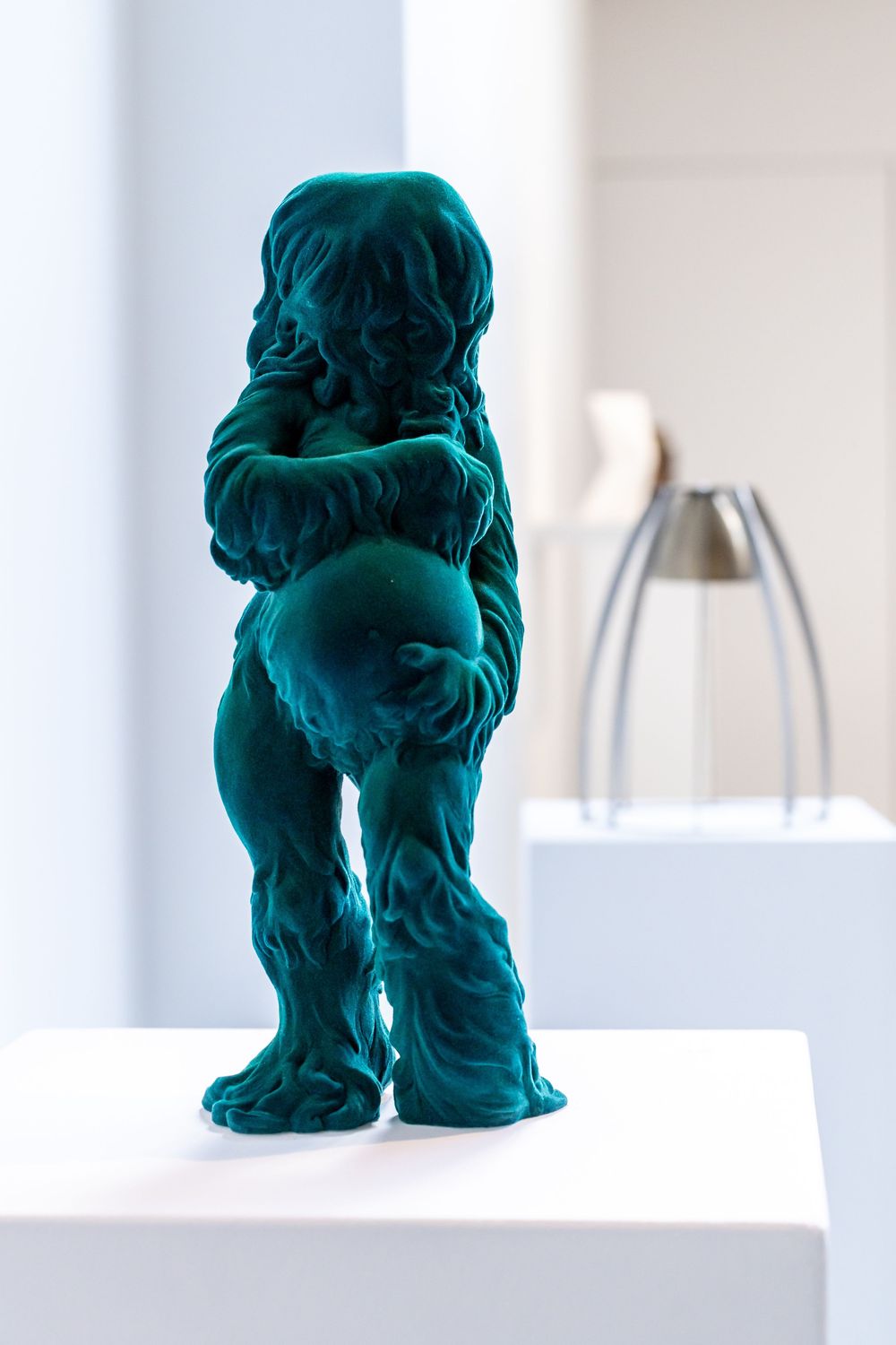 Teal velvet sculpture of a small figure shown from multiple angles against a white background.
