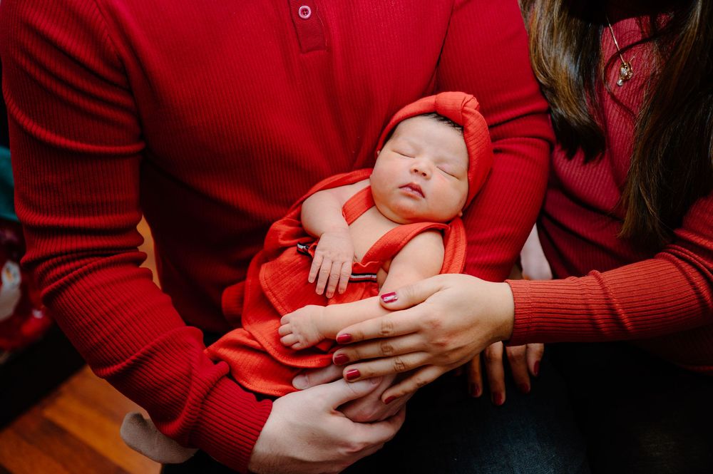 A sleeping baby wearing a red dress is cradled in arms wearing matching red sweaters.