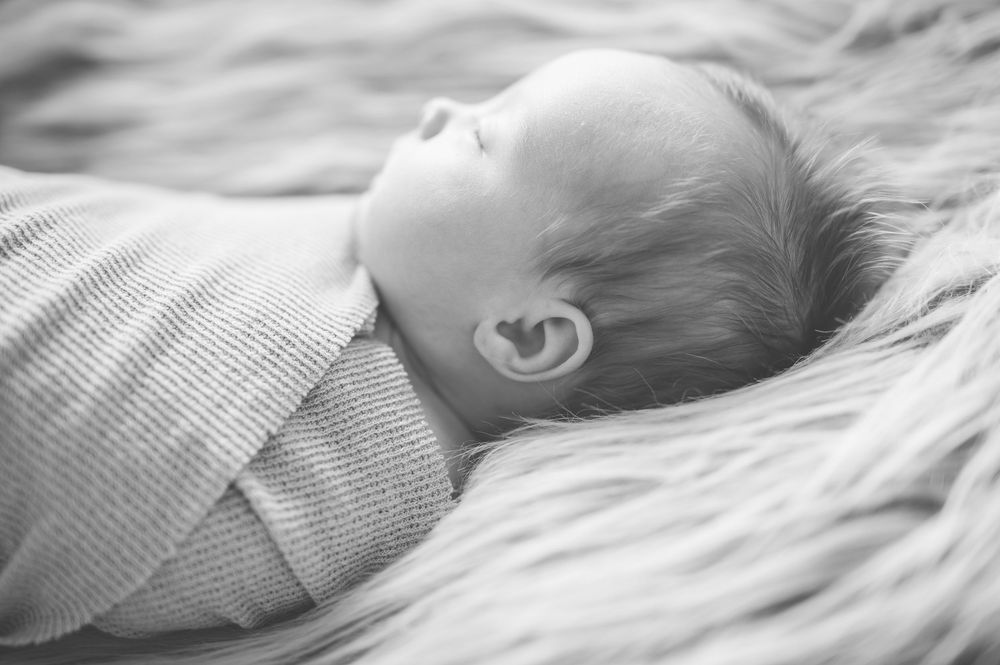 Black and white images of a sleeping infant resting peacefully on soft bedding.