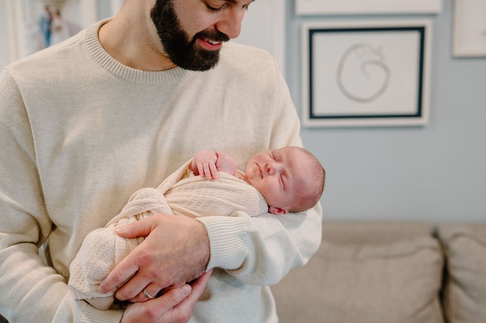 A loving parent holds and comforts their sleeping newborn baby in a peaceful home setting.