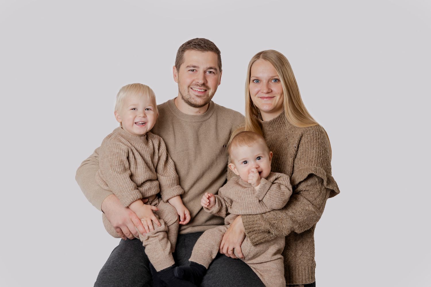 En familie iført matchende beige sweatre sidder sammen foran en lys baggrund til en koordineret portrætsession. Familiefotograf Fyn