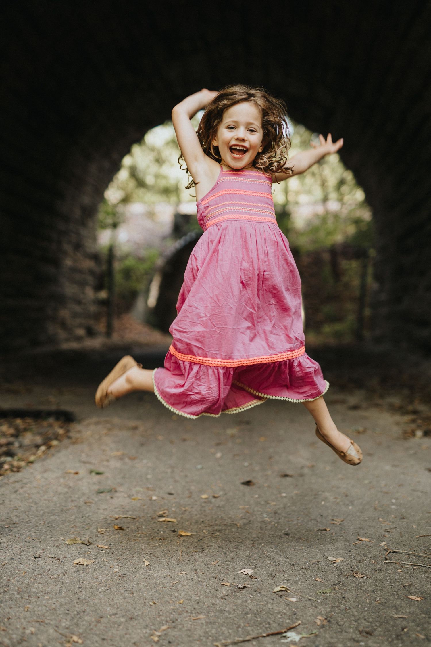 Energetic jump photographed against dark background, pink dress twirling with natural movement and excitement.