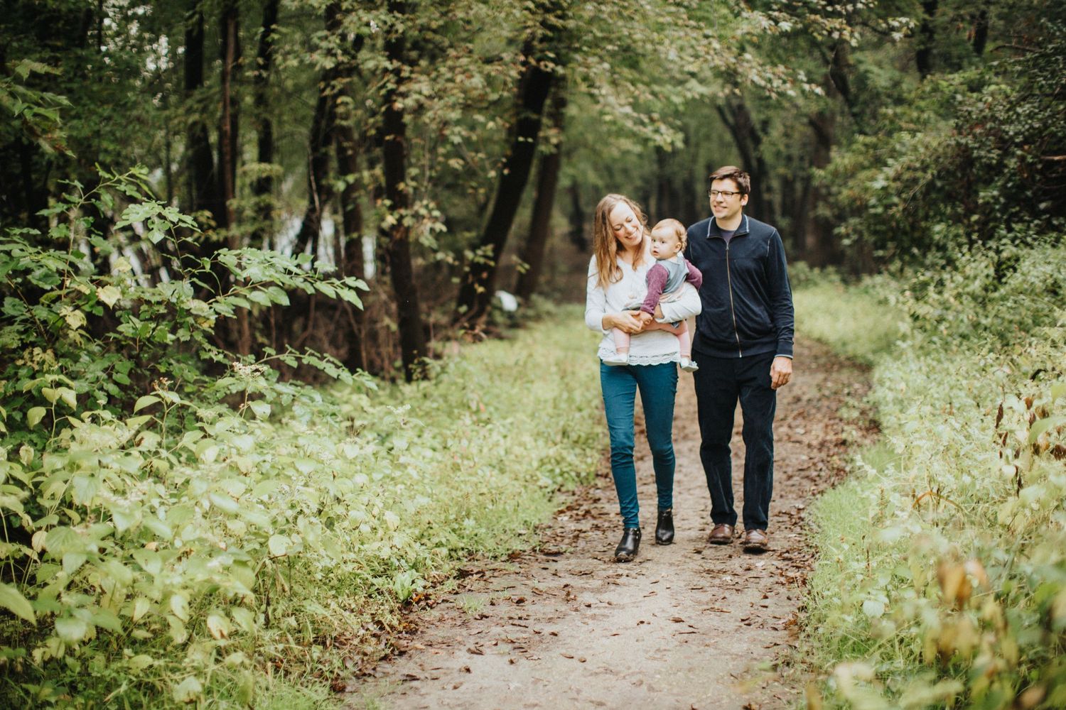 A couple walks hand in hand along a serene wooded trail surrounded by lush green forest on a peaceful afternoon.