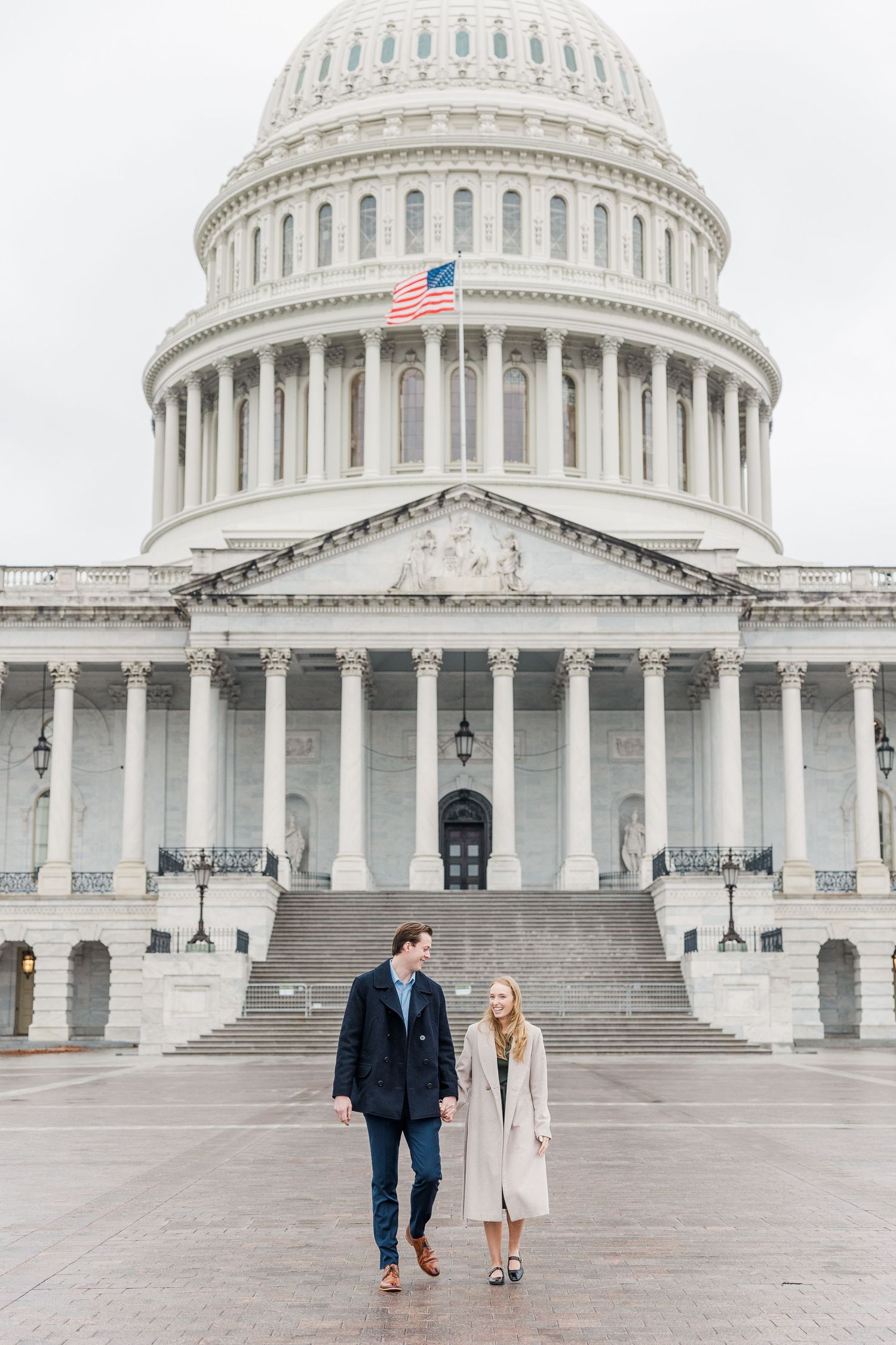 A couple walks together in front of the United States Capitol Building in Washington DC on a cloudy day.