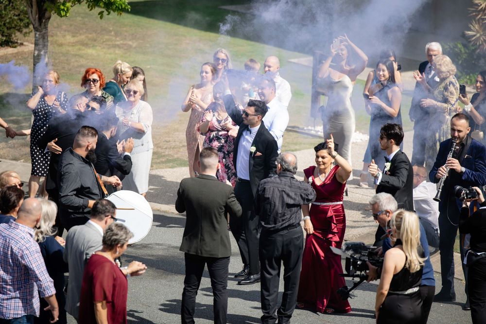 Wedding party celebrating outdoors with smoke effects and live music among guests.