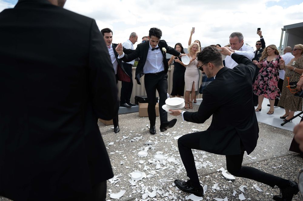 Groomsmen smashing plates in traditional wedding celebration on rooftop venue.