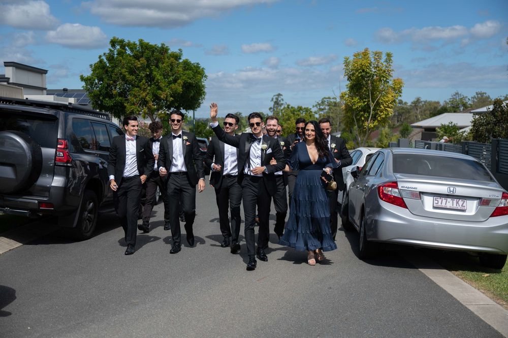 Groom and groomsmen in matching black tuxedos posing together in suburban street.