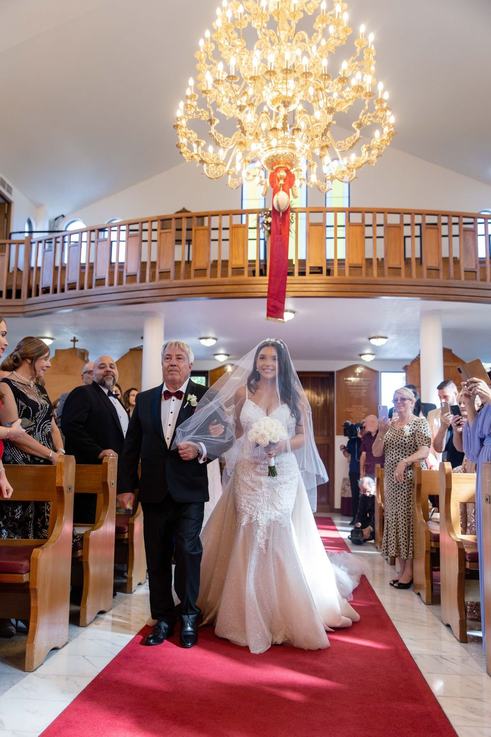 Bride walks down red carpet aisle with father in elegant church.