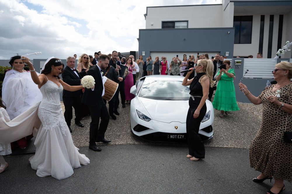 Wedding party poses with white Lamborghini outside modern venue.