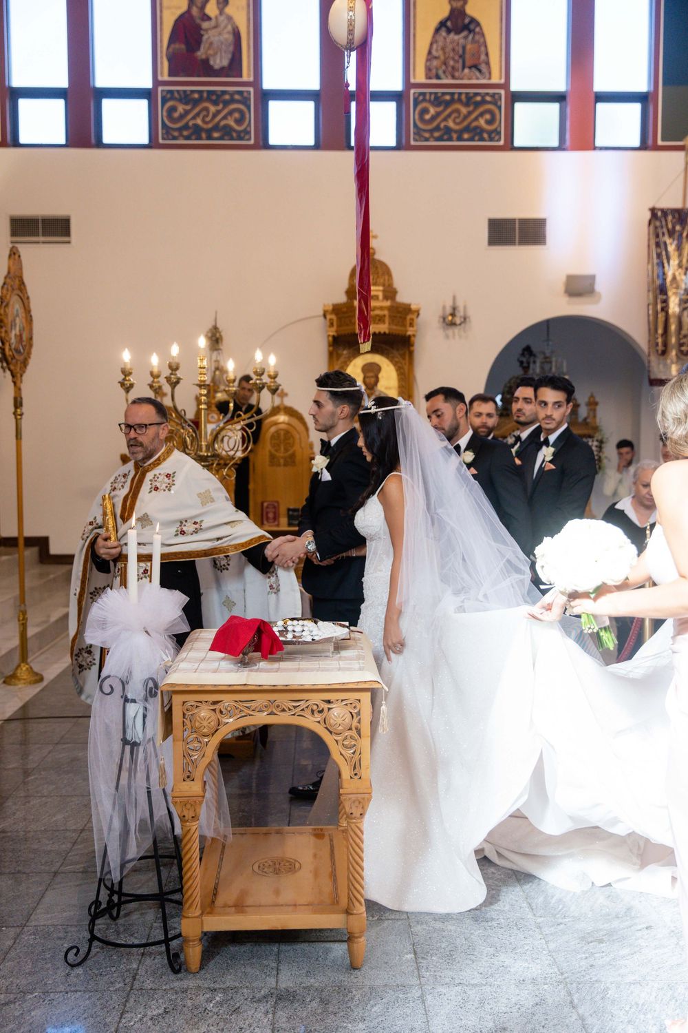 Greek Orthodox priest officiates wedding ceremony with couple at altar.