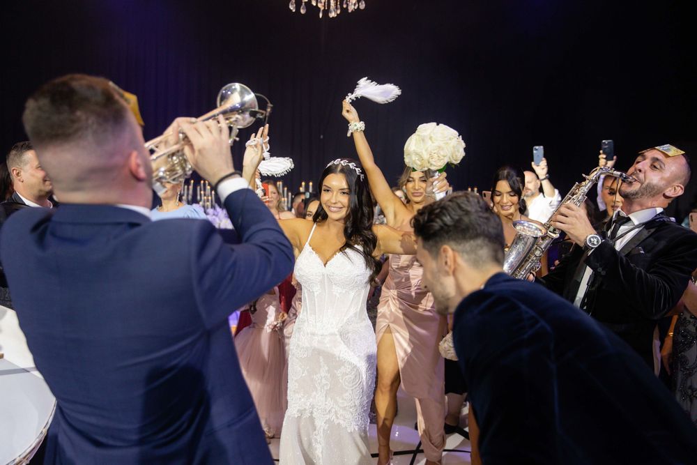 Bride celebrating with guests at wedding reception, raising bouquet while surrounded by cheering crowd.