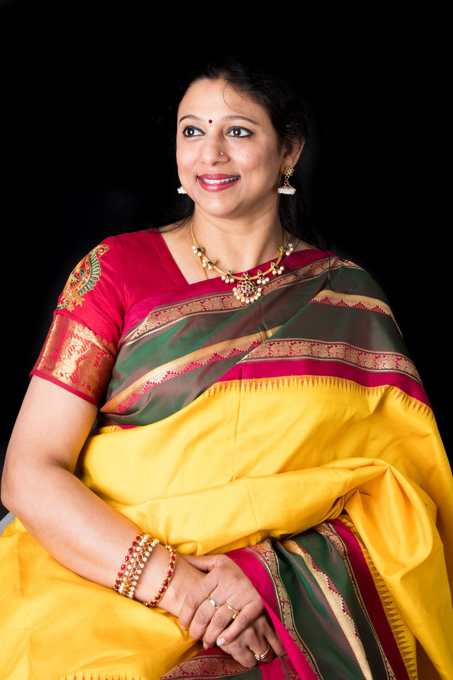 Portrait series of woman in vibrant yellow silk saree with red blouse against dark background.