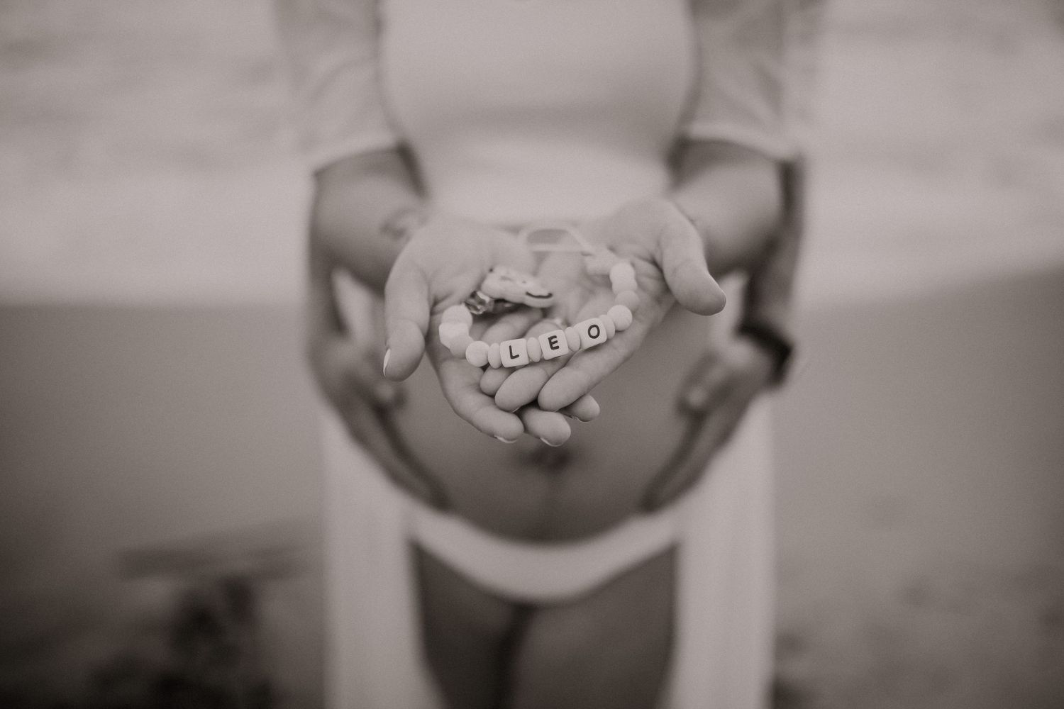 Barriga embarazada en blanco y negro sosteniendo un chupetero con el nombre del bebé