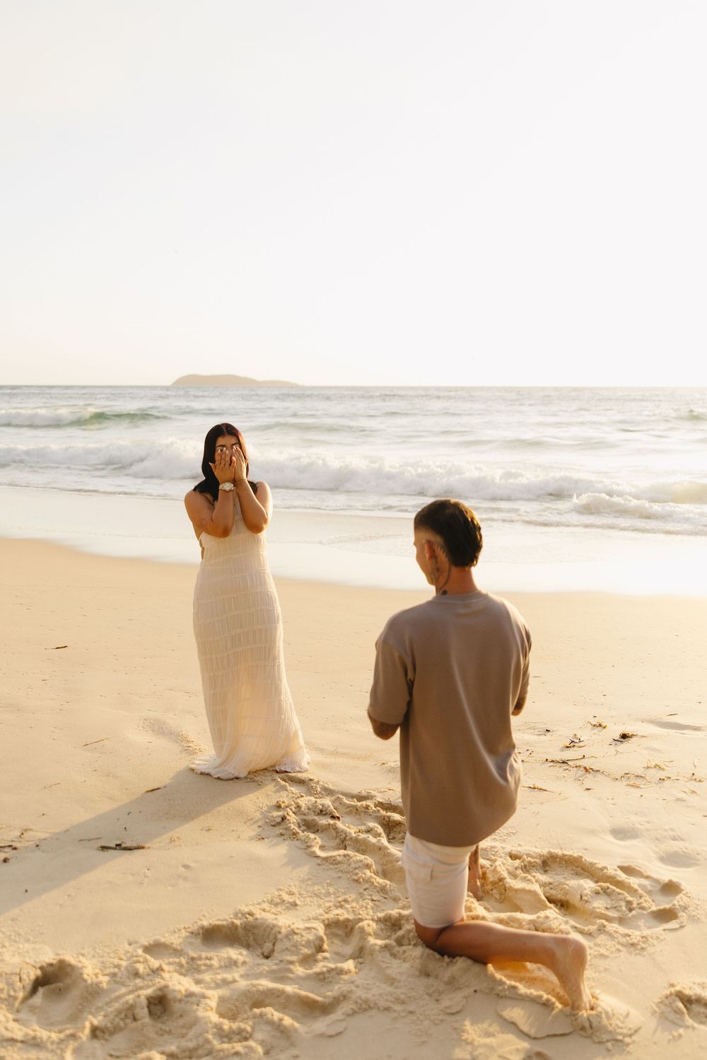 Two people sitting on a sandy beach at sunset looking out at the ocean waves.