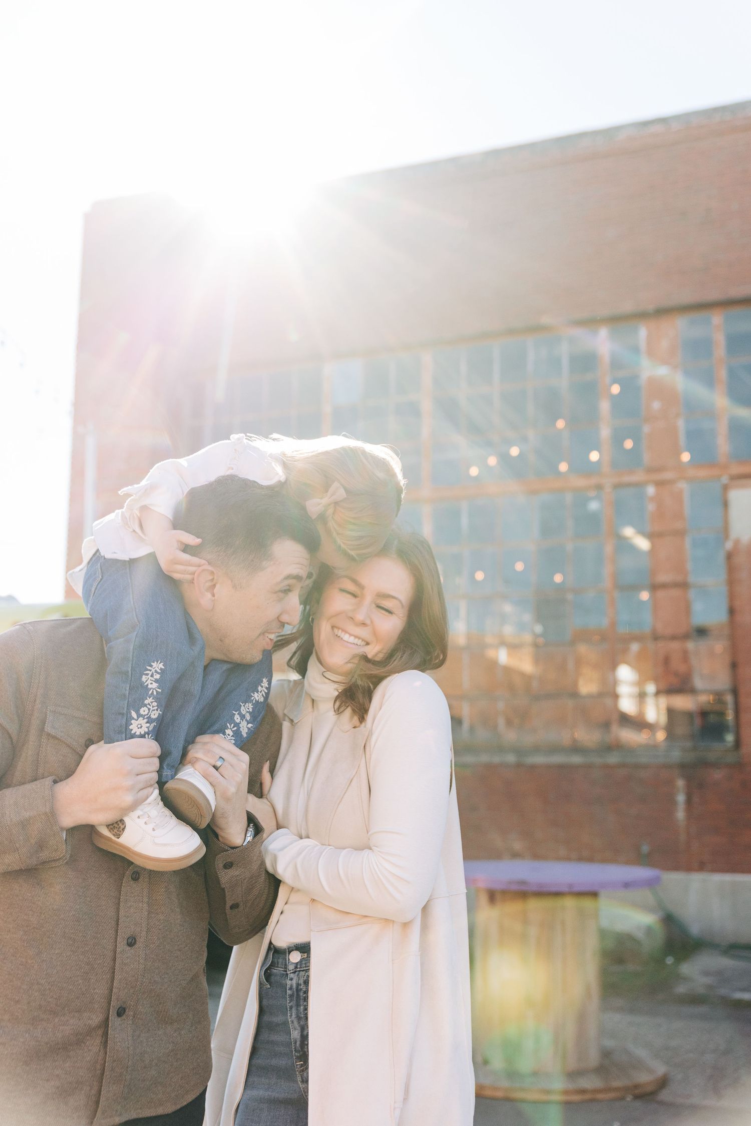 A family shares tender moments in an outdoor photoshoot with sunlit brick buildings in the background in Charlotte.