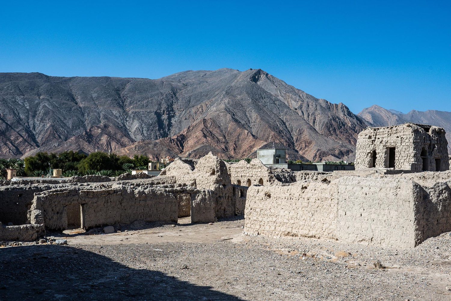 Ancient stone ruins of a fortress stand against rugged mountain landscapes under bright blue skies in Oman.