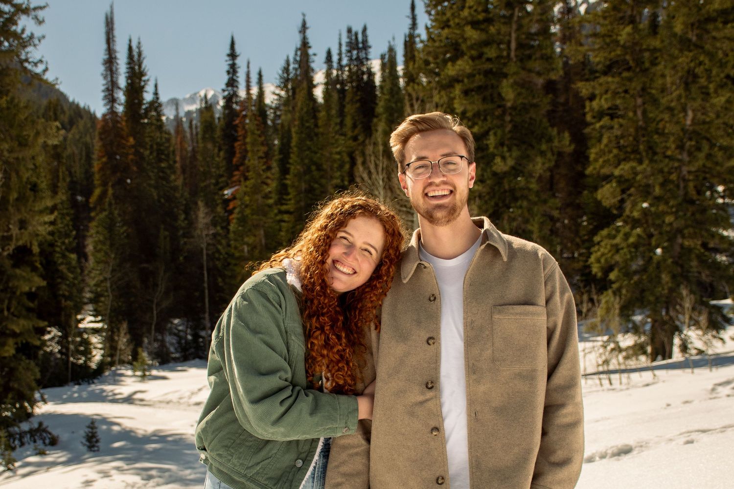 A couple shares joyful moments together while hiking through a snowy winter forest landscape.