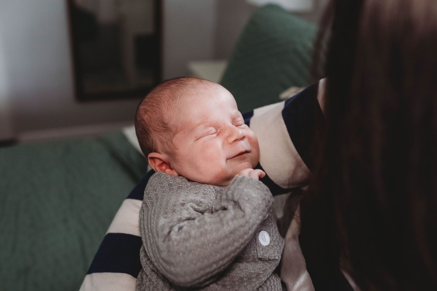 A close-up of a peaceful newborn baby being gently held by a parent in a striped shirt.
