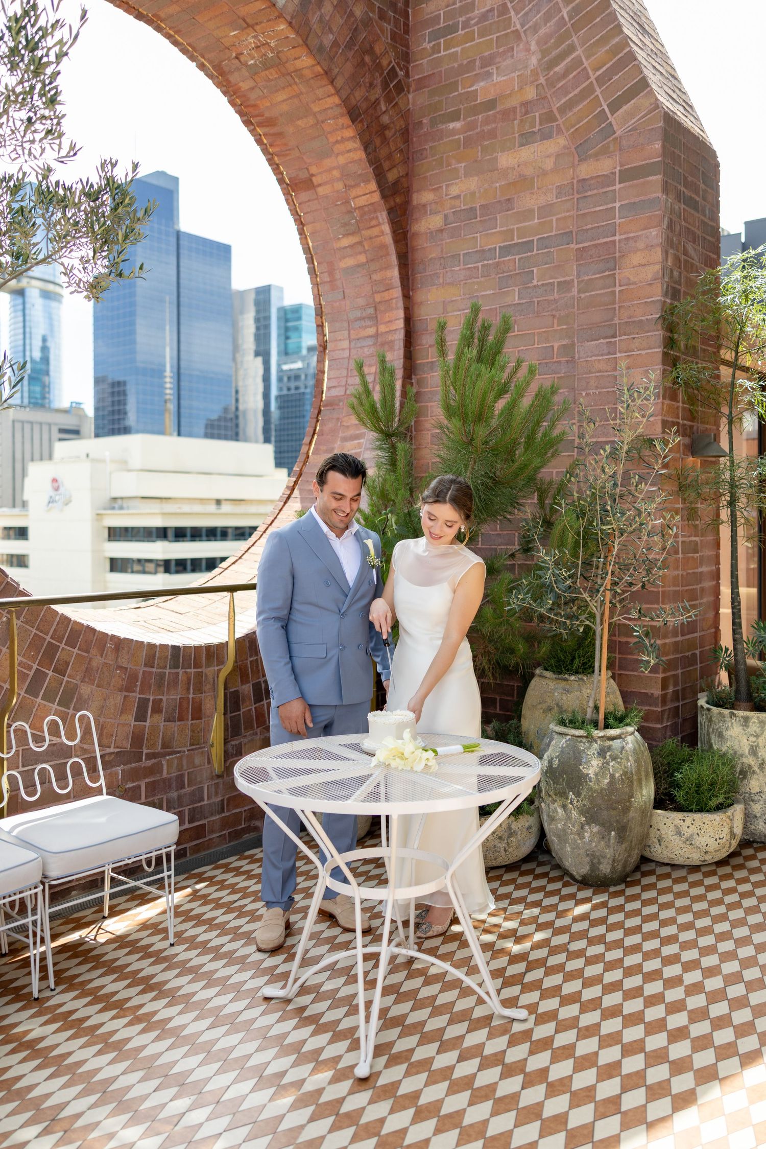 Couple enjoying a romantic moment on a rooftop terrace with brick arches, checkered flooring and city views.