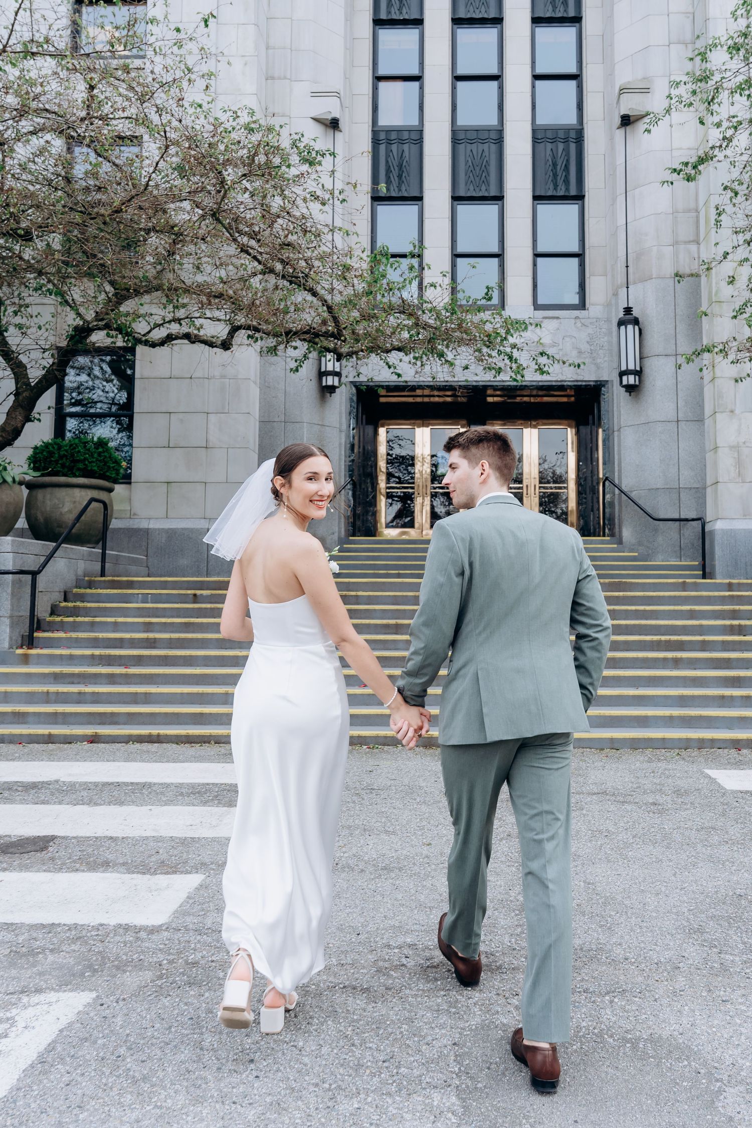 A couple in wedding attire walks away from a stone building with tall windows and steps in a series of progressive shots.
