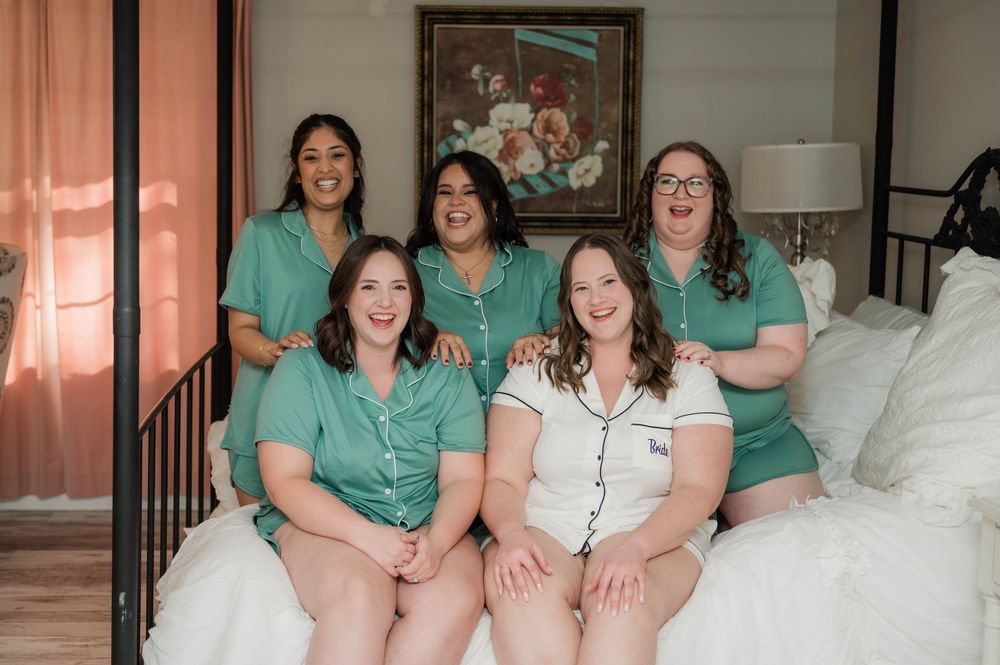 Wedding party members in matching sage green dresses share joyful moments in a bright indoor setting.