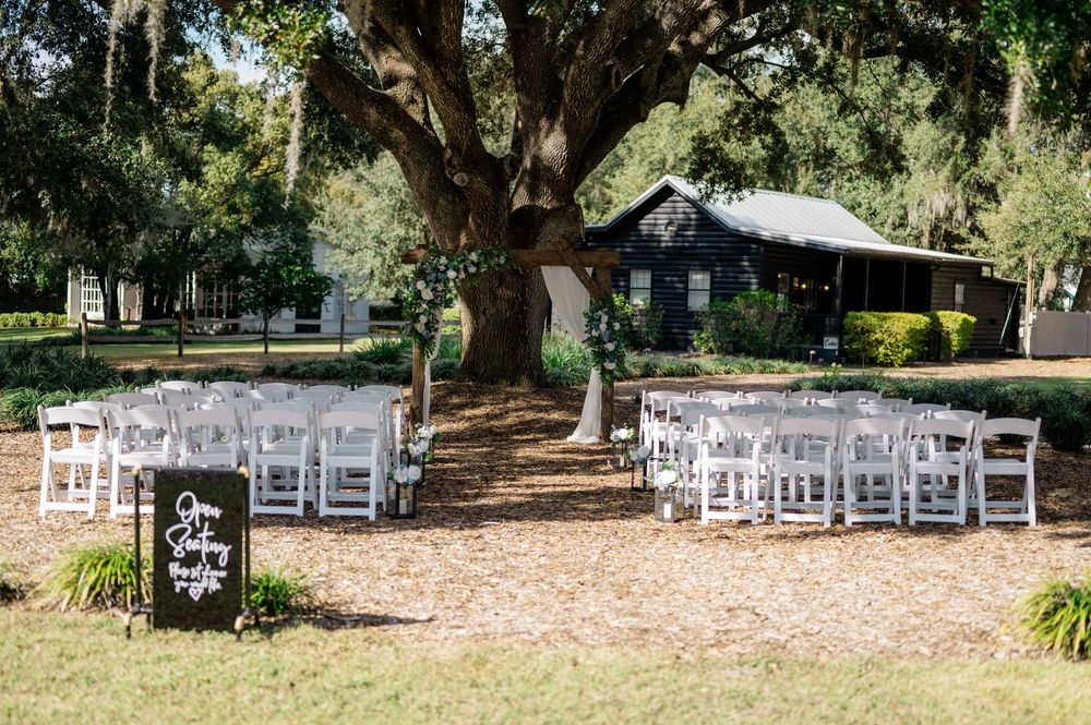 White folding chairs arranged in rows for an outdoor wedding ceremony under shady oak trees.