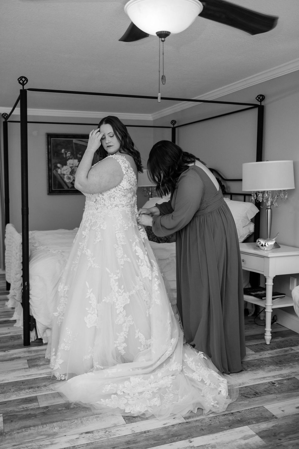 Black and white photo of a bride's wedding dress being adjusted before the ceremony.