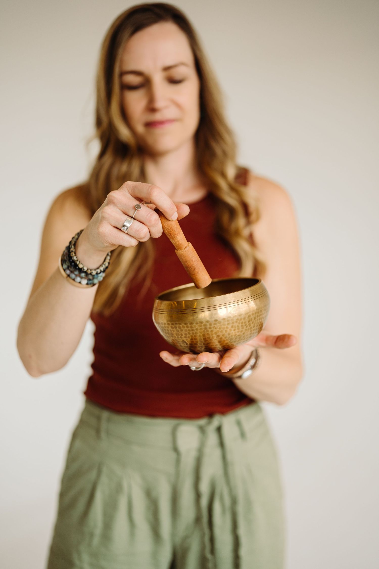 Person in burgundy top and olive skirt holds and plays a Tibetan singing bowl in sequential meditation poses.
