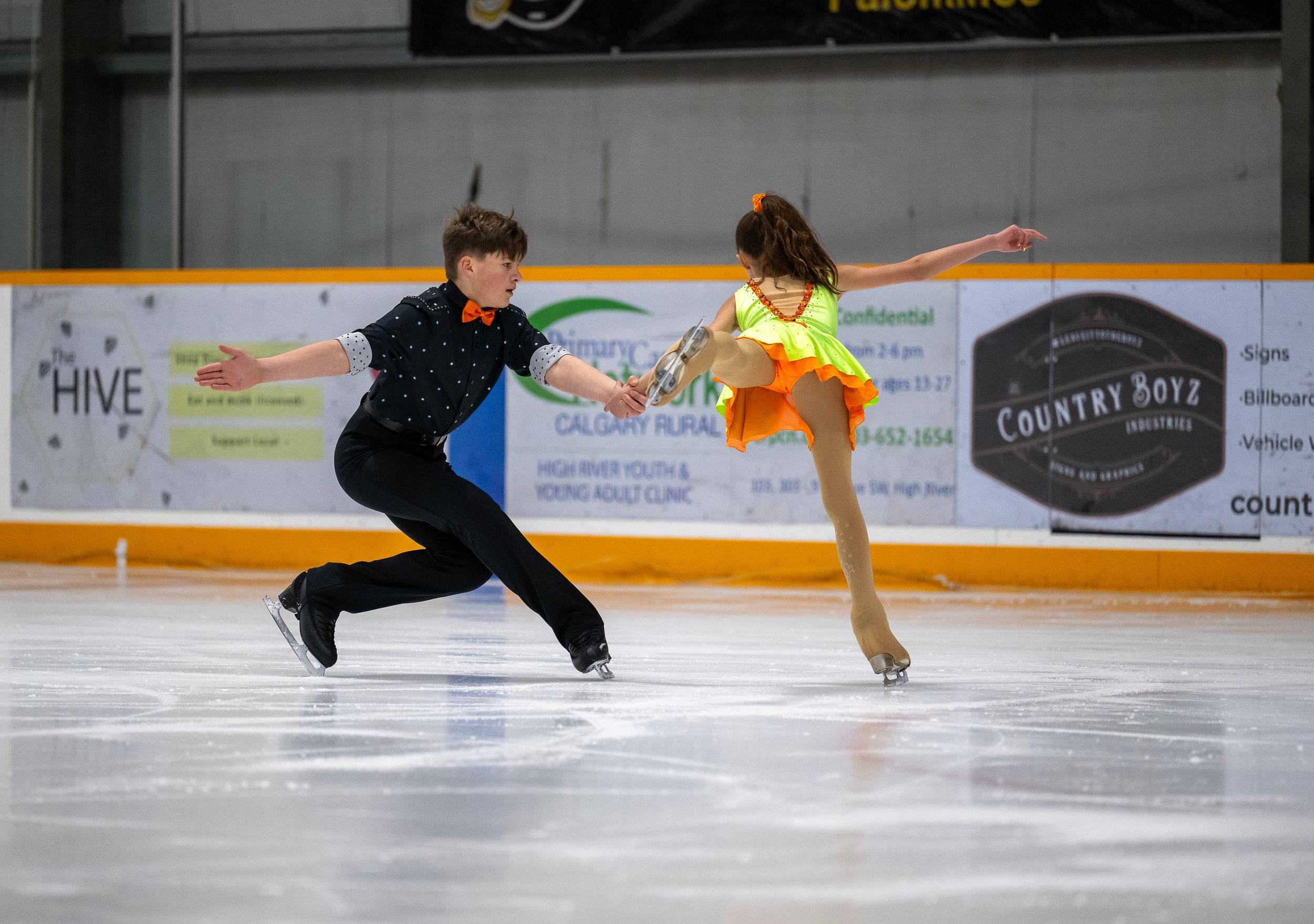 Figure skaters perform jumps and spins in sequence on an ice rink with advertising boards visible in the background.