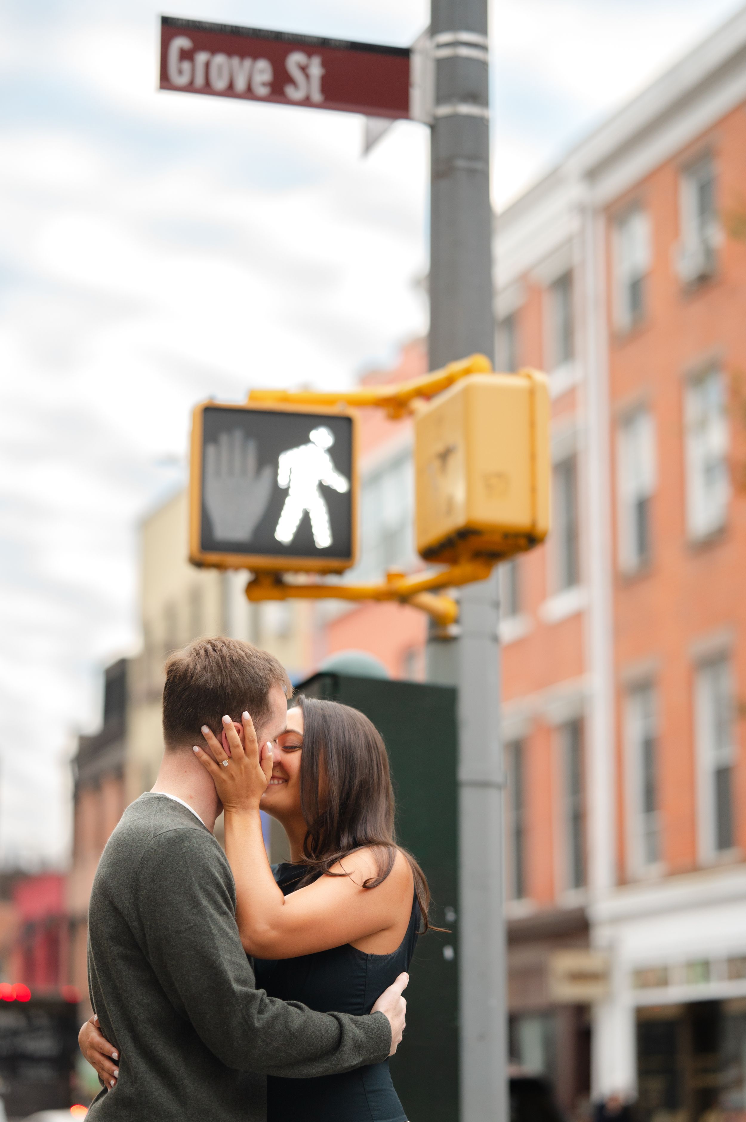 A couple shares a romantic kiss on a city street corner with buildings and street signs in the background.