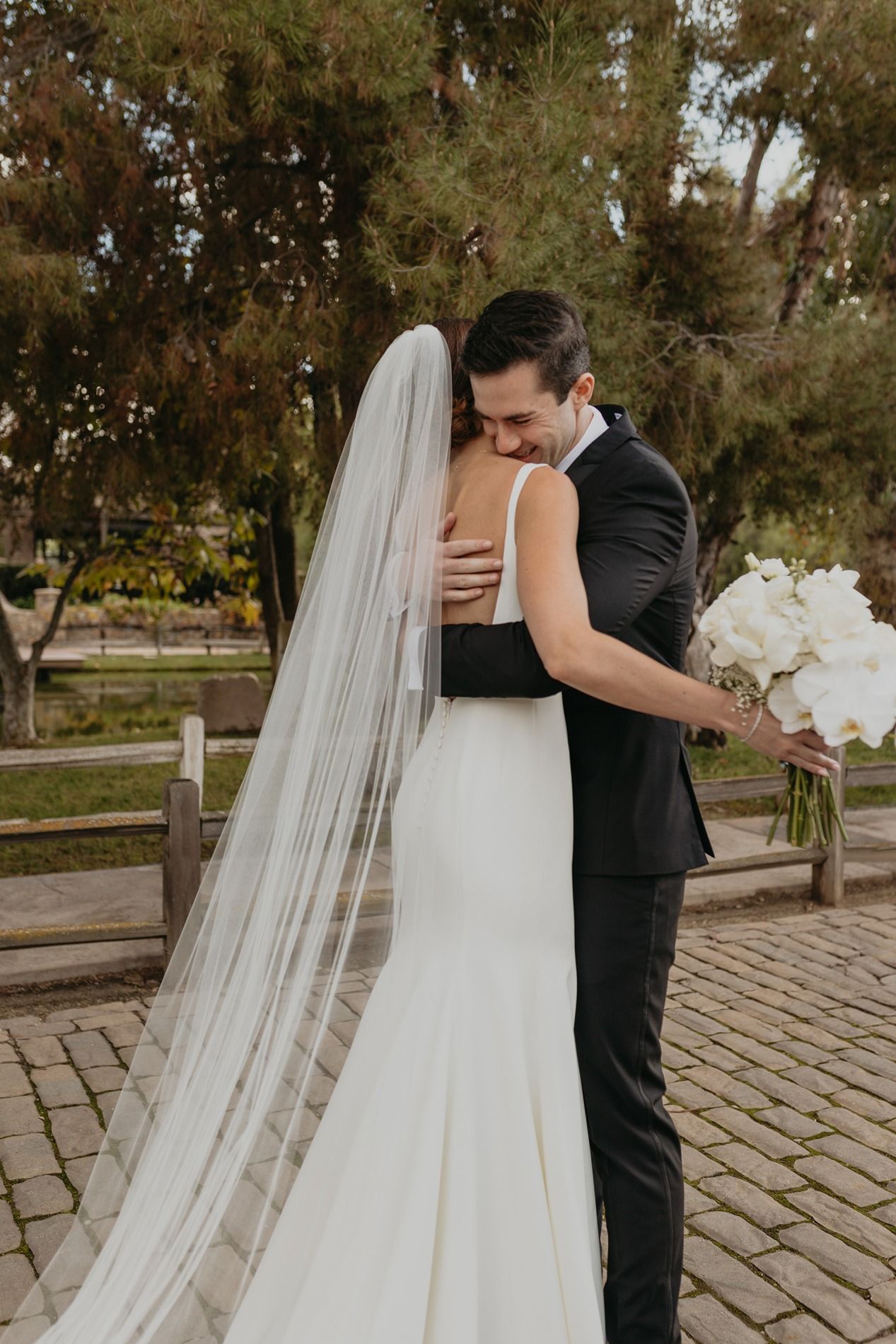 A romantic wedding couple shares intimate moments on a stone patio surrounded by trees at Lake Oak Meadows in Temecula.