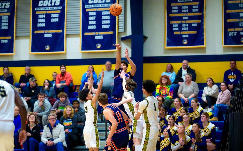 Hershey Trojans player leaps for a layup with teammates and fans watching in the packed gym by SportsFox Photography, Hershey PA.