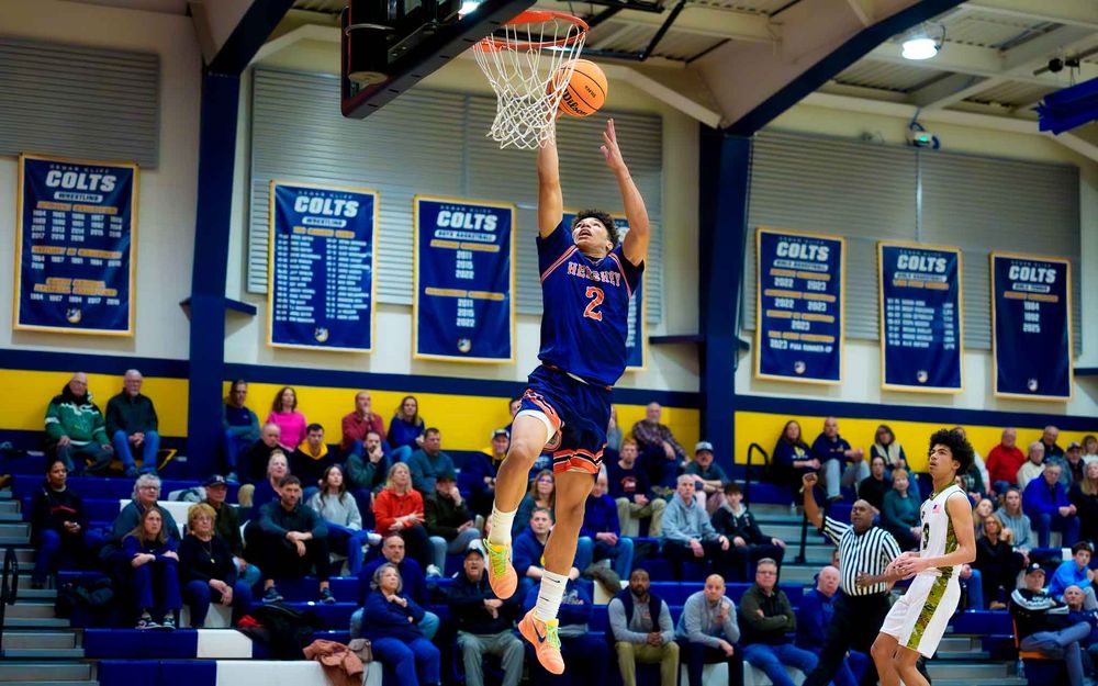 Hershey Trojans player jumps for a layup with the crowd and banners visible in the background by SportsFox Photography, Hershey PA.