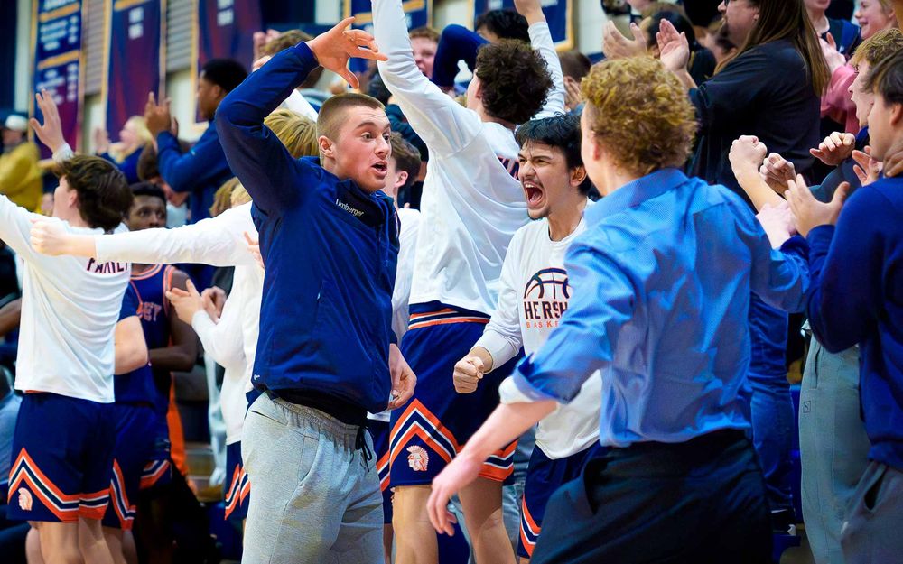 Hershey Trojans players & fans leap up from the sidelines, cheering and raising their arms in celebration by SportsFox Photography, Hershey