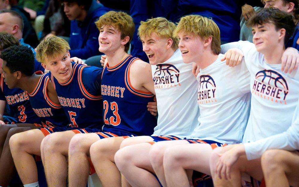 Hershey Trojans bench players sit together, smiling and celebrating with arms around each other by SportsFox Photography, Hershey PA.
