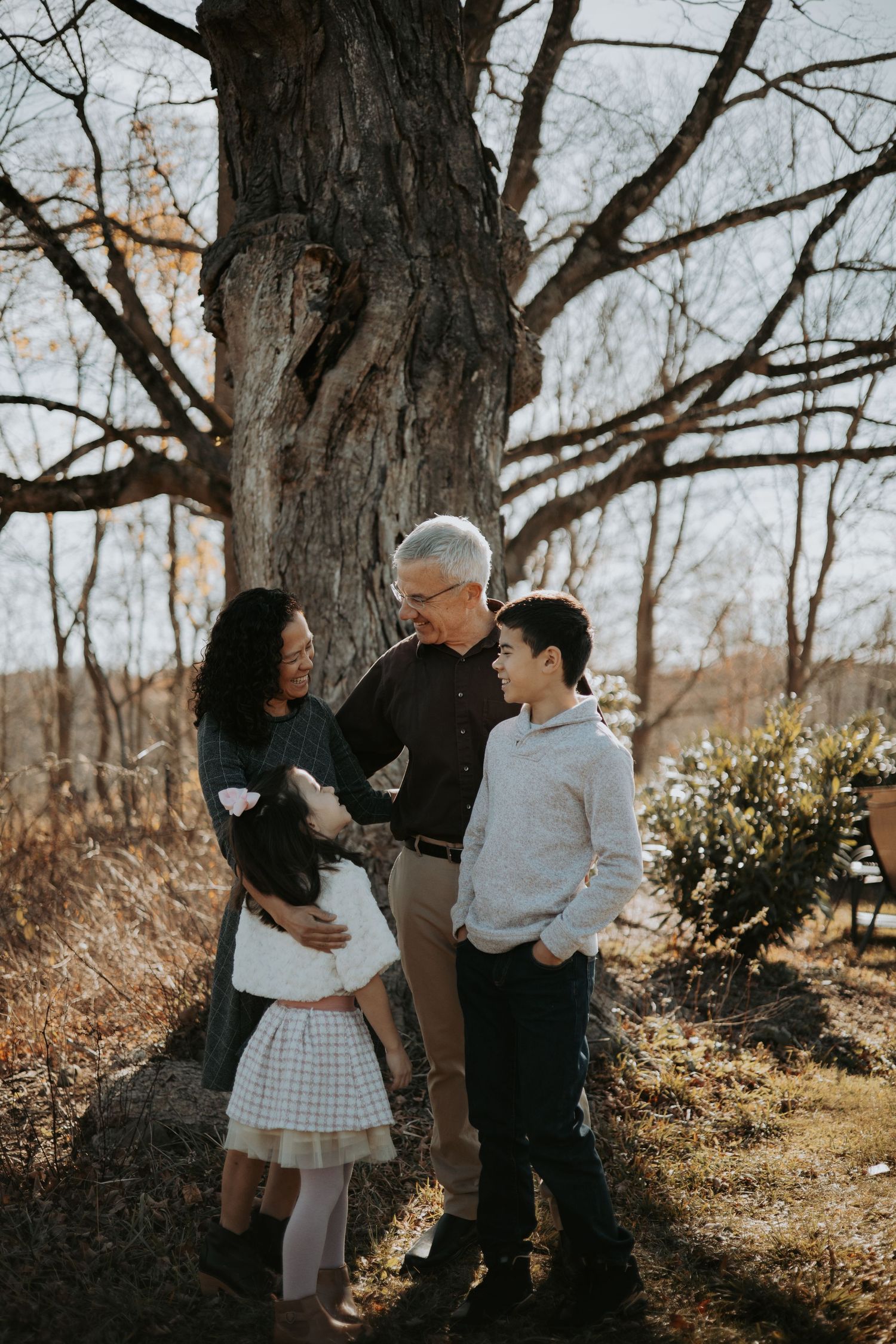 Family sharing a tender moment together in a wooded area during autumn with bare trees in the background.
