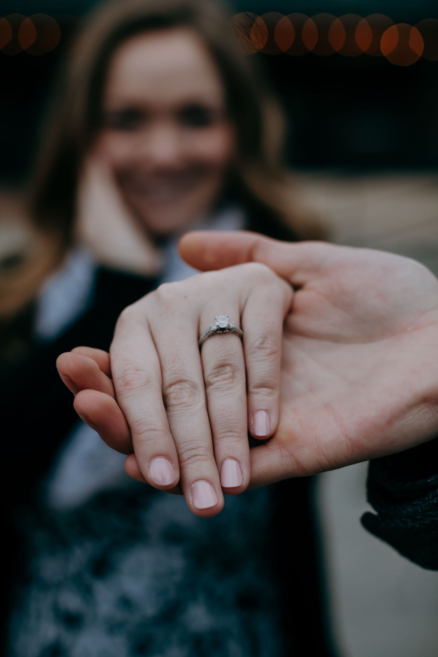 Close-up of engagement ring on woman's hand held by partner.