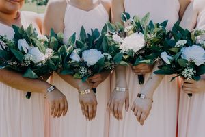Bridesmaids in blush pink dresses holding lush white and greenery wedding bouquets with delicate wrist corsages.