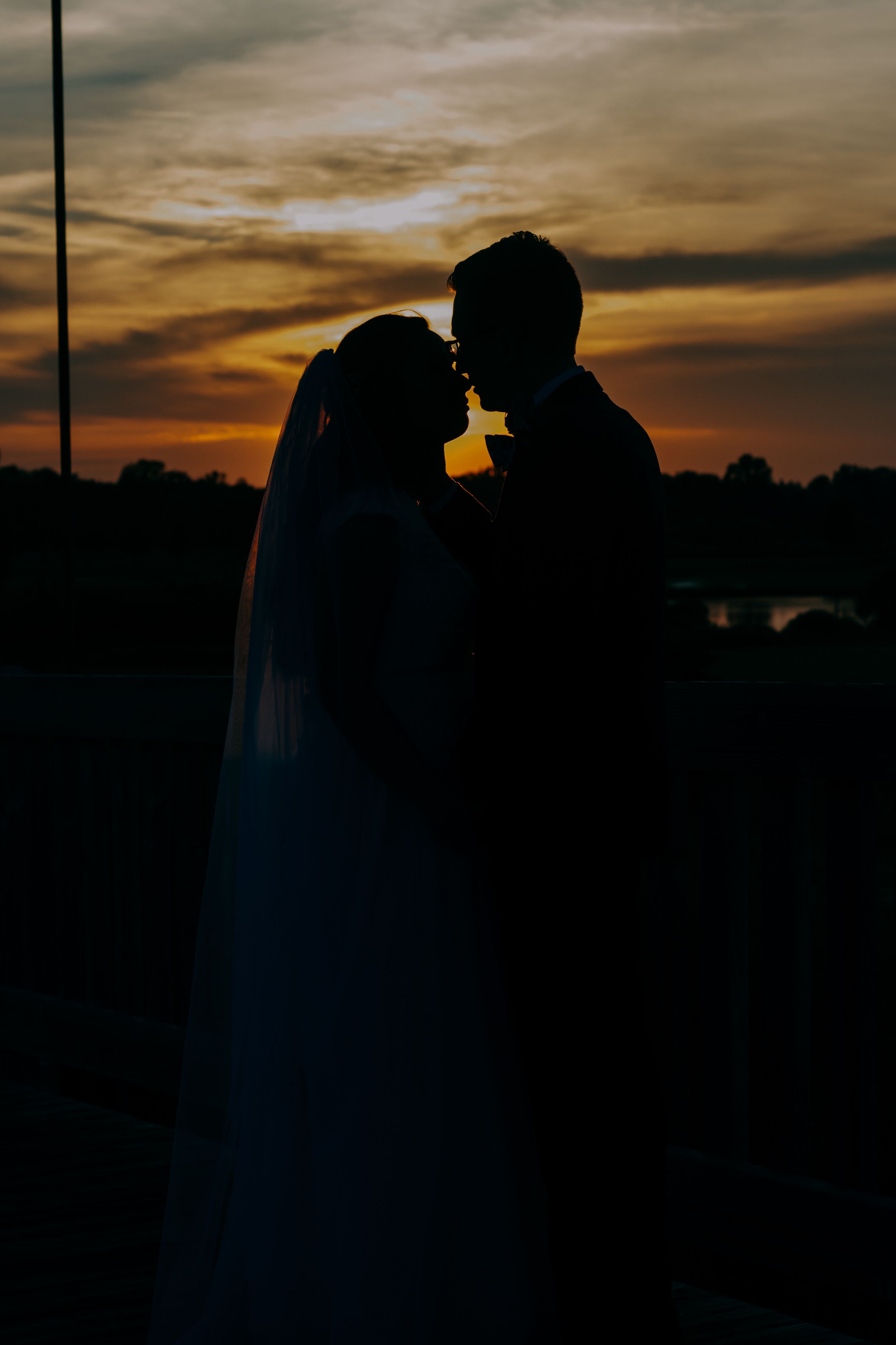 Romantic silhouette of bride and groom sharing a kiss against a stunning golden sunset sky.