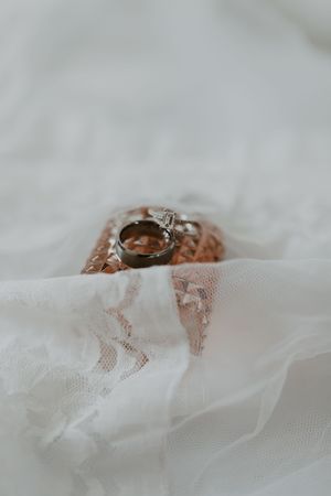 Wedding rings and diamond engagement ring displayed on rose gold box atop delicate white lace fabric.