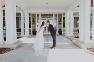 Bride and groom share a romantic kiss under white columns at the entrance of an elegant wedding venue.