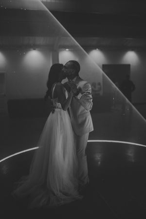 Black and white photo of bride and groom sharing first dance, illuminated by spotlight in elegant reception venue.