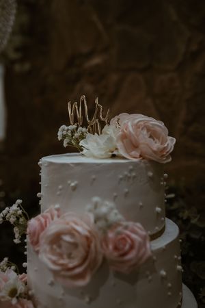 Elegant two-tier white wedding cake decorated with pink roses and gold Mr and Mrs cake topper.