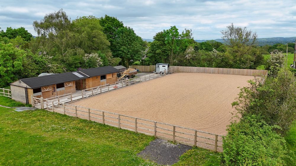 Panoramic landscape of a fenced equestrian arena surrounded by green countryside.