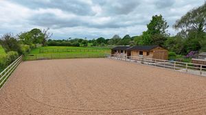 Wide view of a sandy horse riding arena with wooden fencing under cloudy skies.